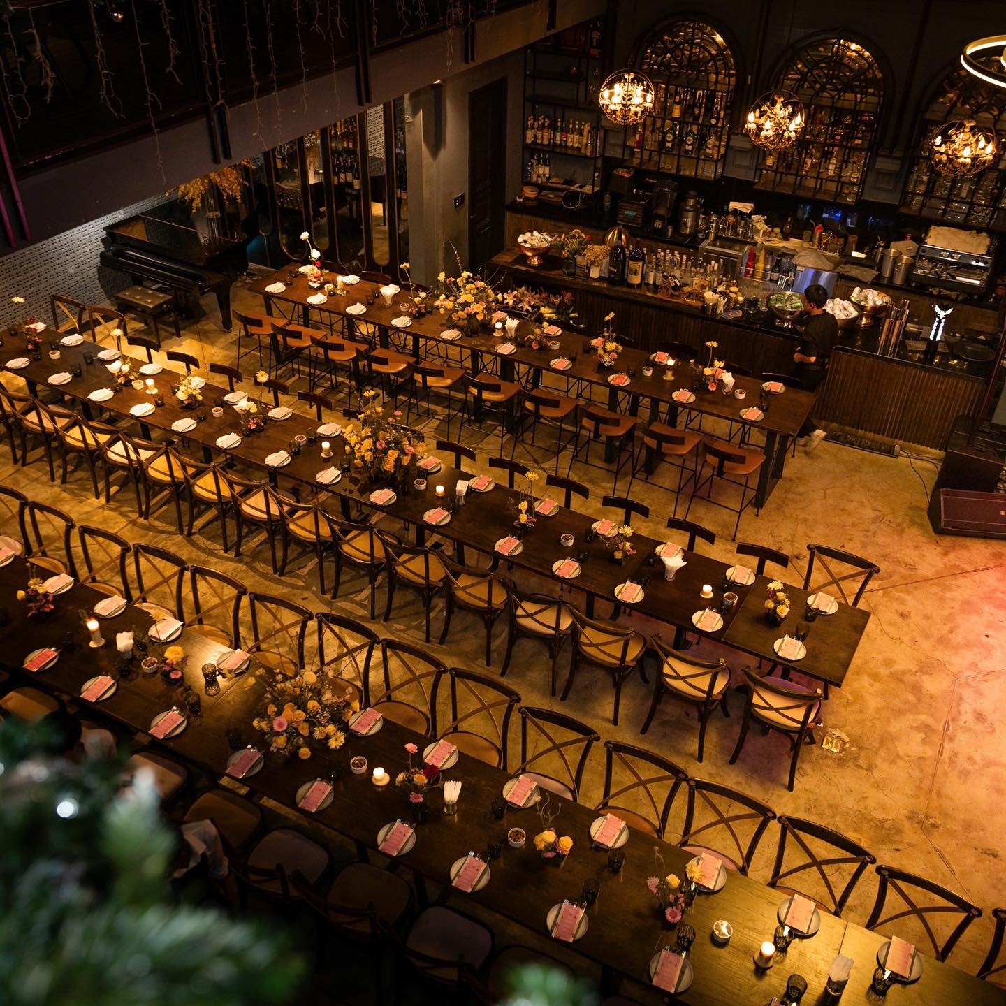The OX dining room with long wooden tables, flowers, amber chandeliers, a bar and a piano