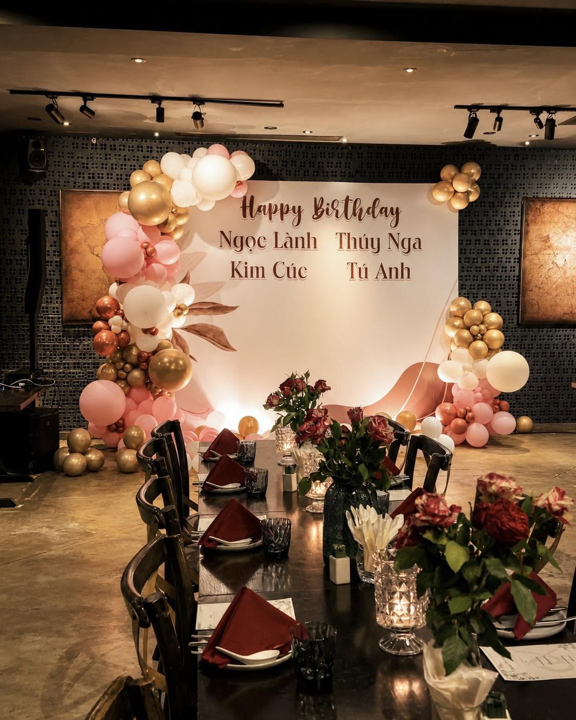 An empty birthday banquet table with roses and a pink-and-gold balloon backdrop