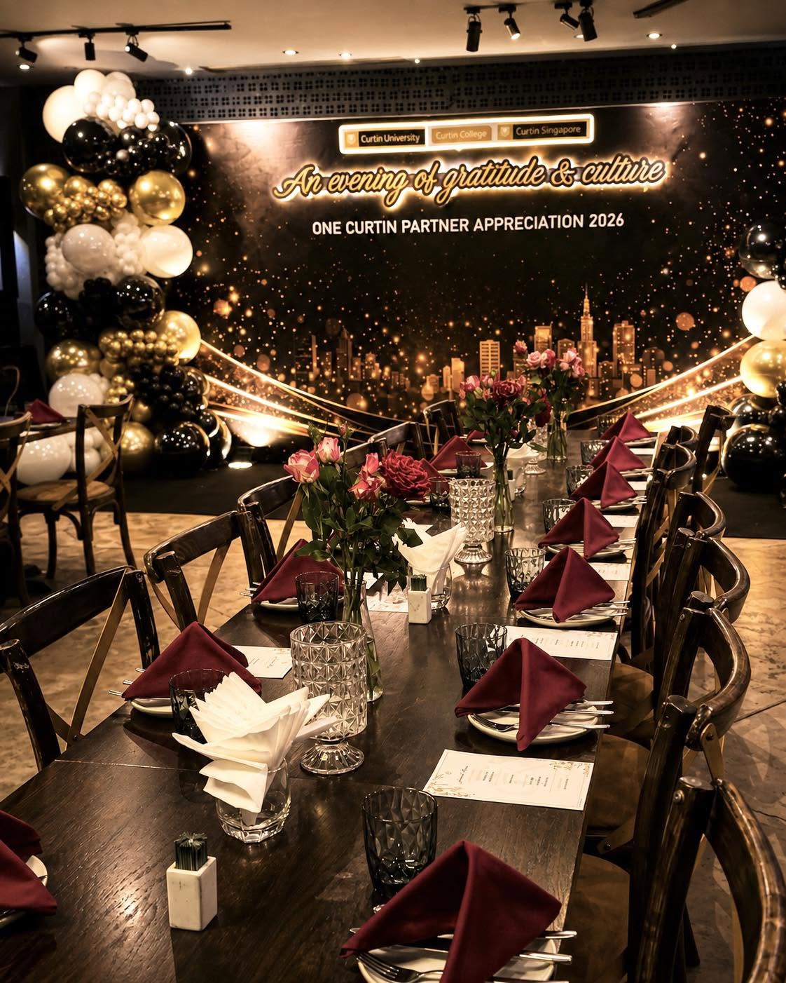 A business appreciation dinner setting with a branded backdrop and floral tables