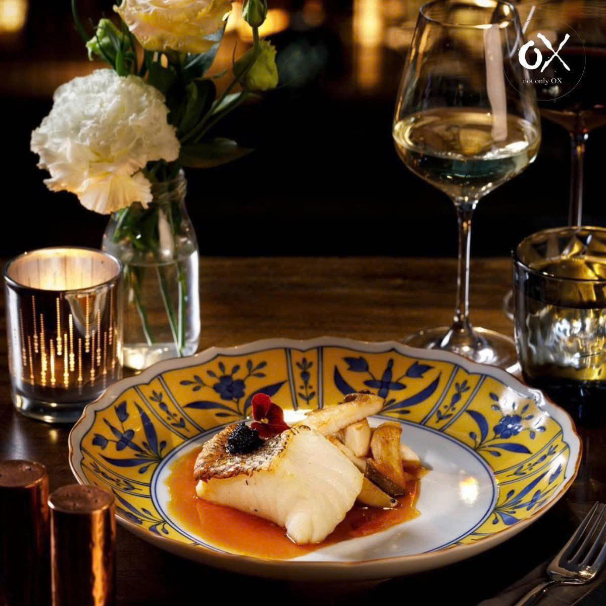 A fish dish with sauce and a flower on a blue and yellow plate