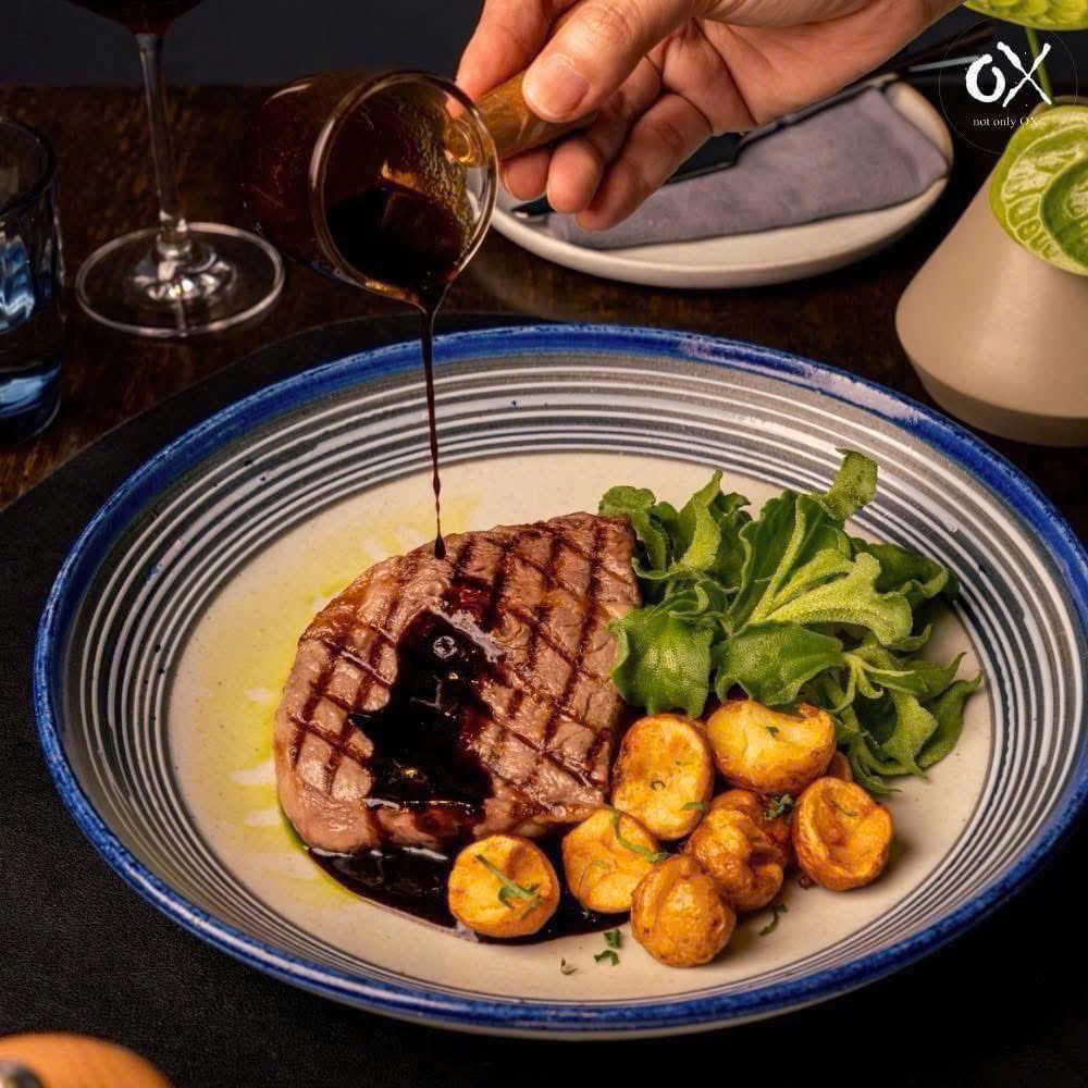 Sauce being poured over grilled meat with potatoes and rocket
